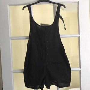 Black romper with pockets in front, button accents, and ties on shoulders.